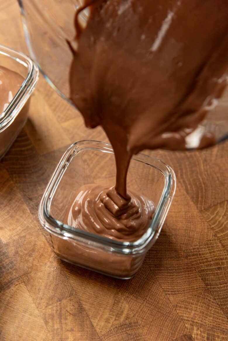 Pouring thick creamy silken tofu chocolate mousse from the blender into a small glass container.