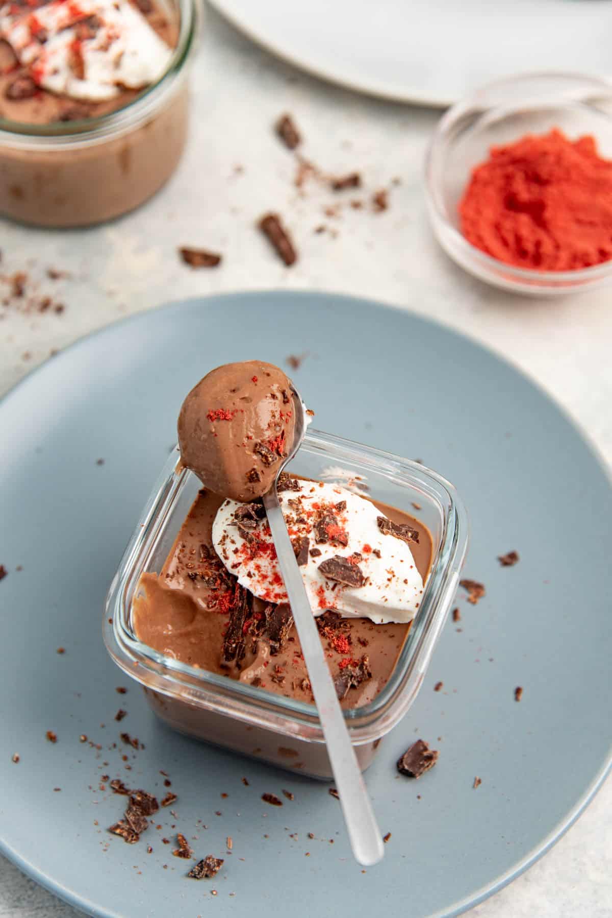 Close up of a spoonful of protein chocolate mousse sitting on top of a glass container of mousse.