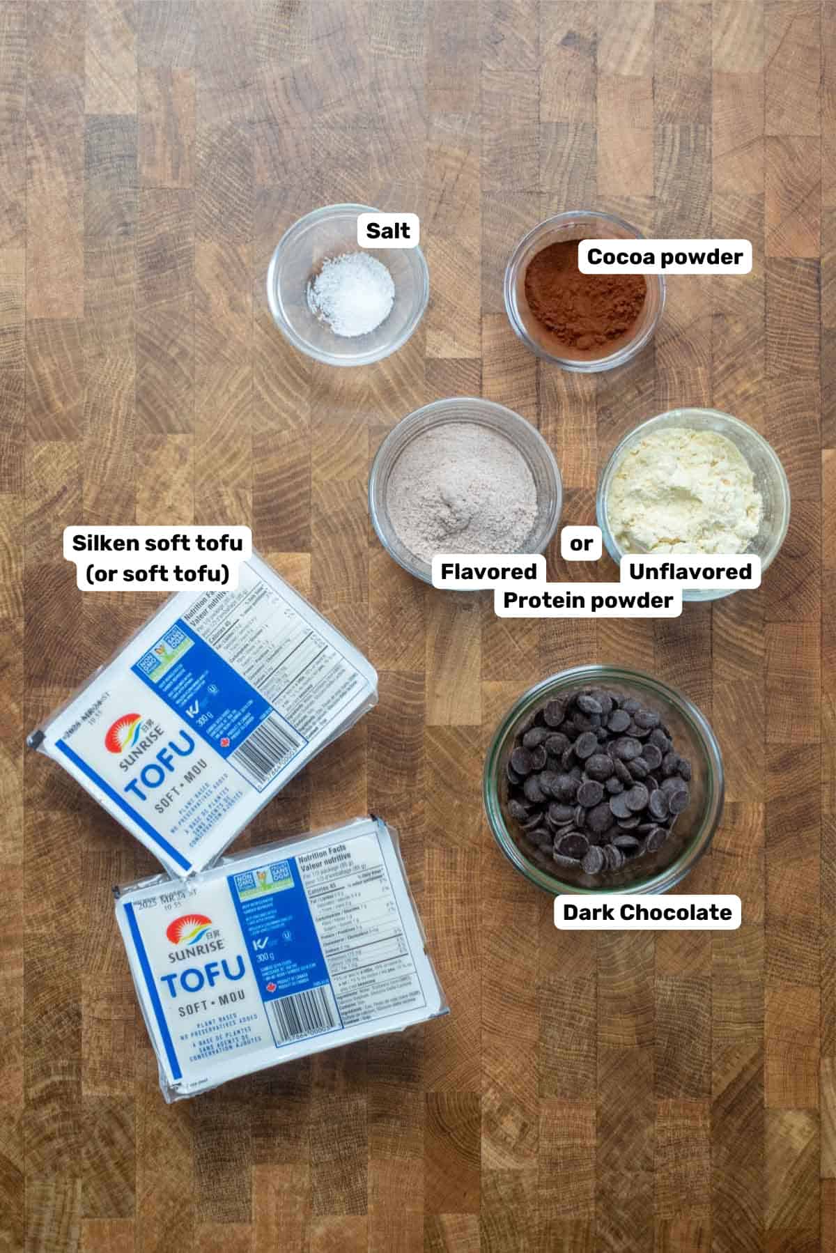 Labeled ingredients to make high protein tofu chocolate mousse on a wooden table.