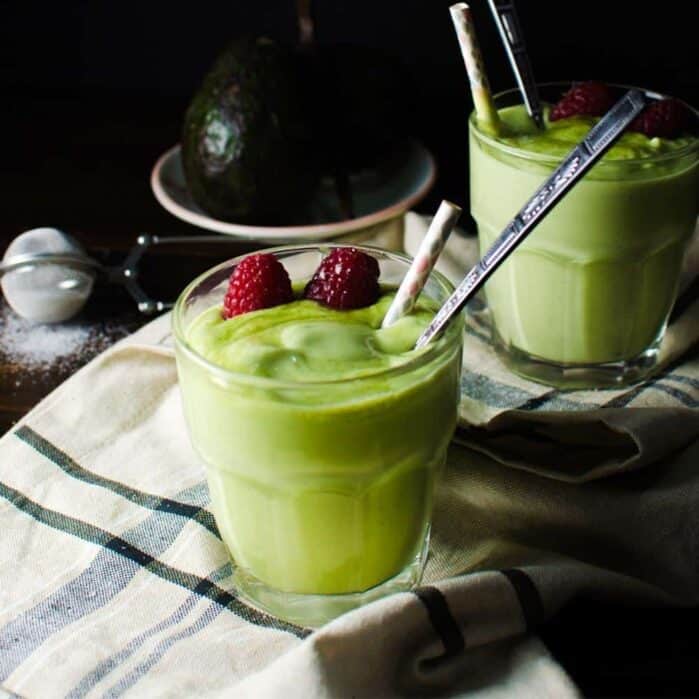 Creamy green vanilla avocado drink in a glass, served with a straw and a spoon.