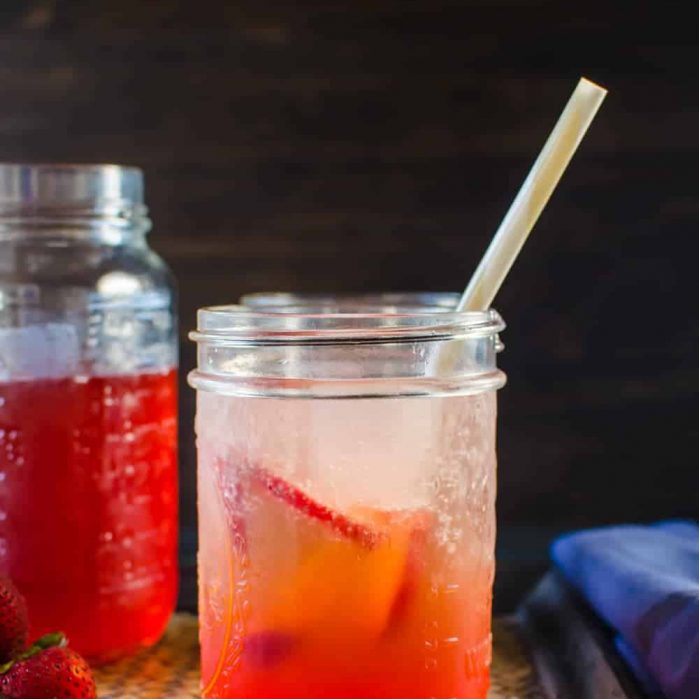 Vanilla strawberry shrub served in a glass jar with a straw and strawberry slices in the drink.