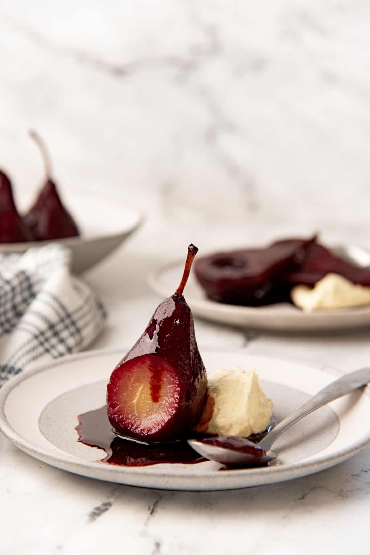 Red wine poached pear on a grey plate with the side sliced to show the interior of the poached pear.
