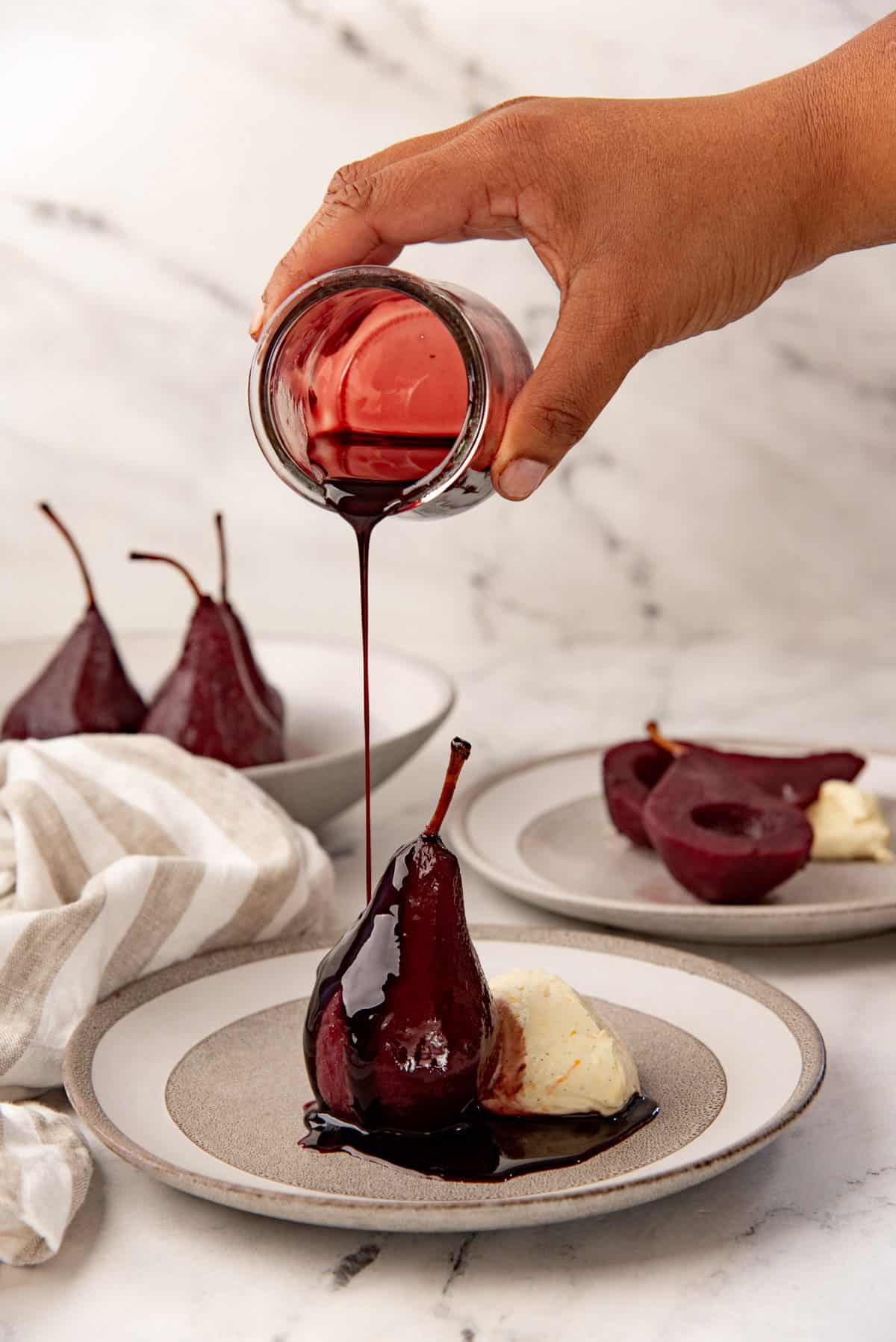 Red wine poached pear served with mascarpone on a plate, with the wine syrup being poured on top.