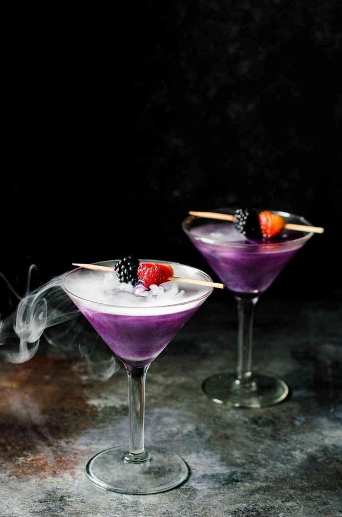 A martini glass with a bright purple drink, silvery white shimmery swirls, and smoke from dry ice.